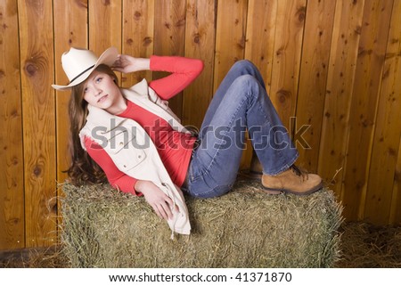 A woman laying on a hay bale with a white hat on with a serious look on her face,