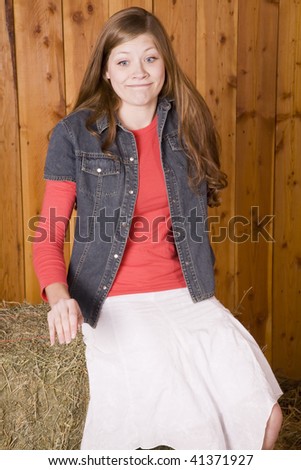 A woman sitting on a bale of hay with a goofy look on her face.