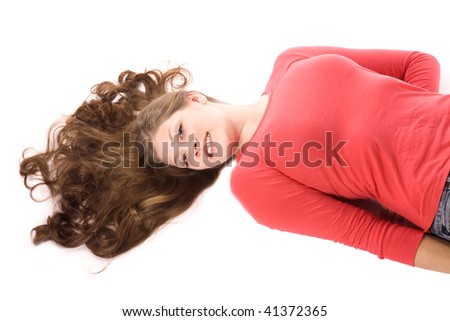 A woman laying on her back with her hair fanned out with a red shirt on and denim pants smiling.