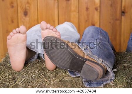 A couple with their feet stacked together on a hay bale.