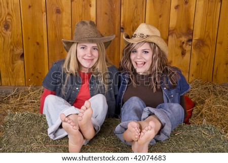 two friends sitting with their feet up on a bale of hay with hats on and big smiles.