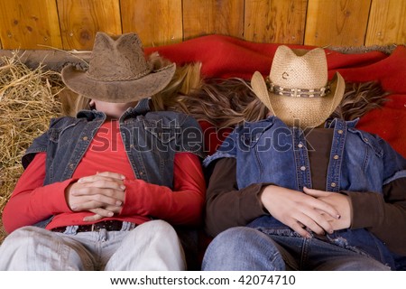 Two friends laying on a red blanket with hats on their faces relaxing.