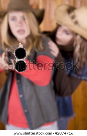 Two teen pointing a shot gun with angry expression on her face with her friend scared.