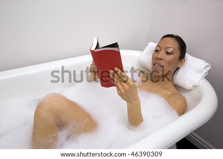 A woman sitting in her tub full of bubbles relaxing while she reads a good book.