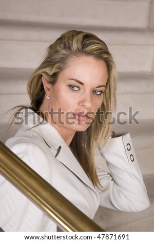 a woman sitting on her stairs after work relaxing and fixing her hair with a sad expression on her face.