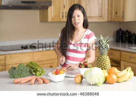 A woman in her kitchen with vegetables and fruit all around her with a big smile on her face.