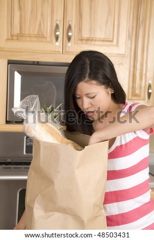 A woman in her kitchen reaching into her bag of groceries.