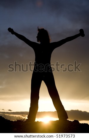 A silhouette of a woman with her arms stretched out holding weights with a beautiful sunset.
