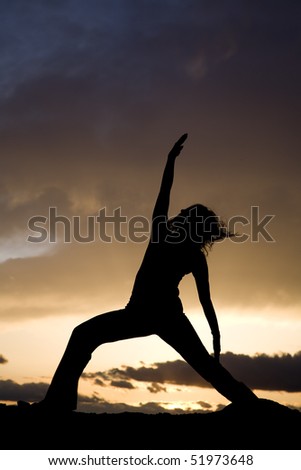 A silhouette of a woman doing a yoga pose on the beach with a sunset behind her.