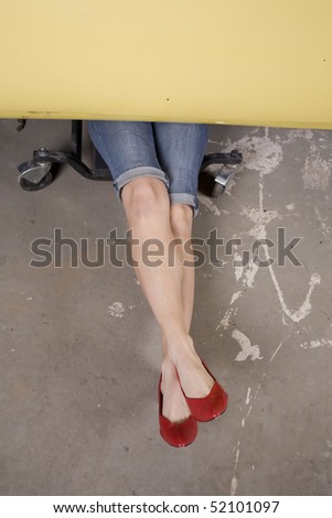 A woman in her red high heels laying under her car trying to fix a problem.