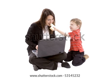 A mom is working on her computer while her son gives her a bite of his sandwich