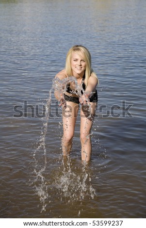 A woman playing in the water by splashing and throwing the water in the air.