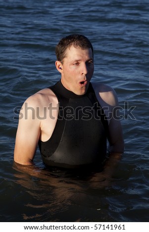 A man wearing his wet suit showing the expression of how cold the water is.