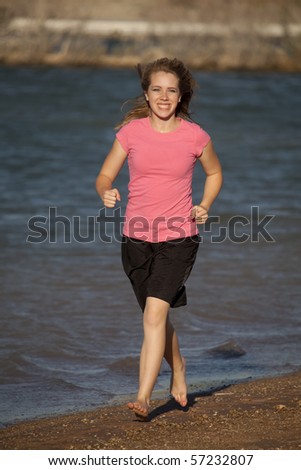 A young teenager in a pink shirt and black shorts running barefoot on the beach.