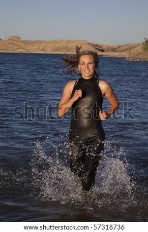 A woman in her wet suit running in the water getting ready to dive in.