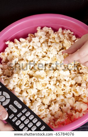 A close up of a remote for the tv and a persons hand reaching for some popcorn.