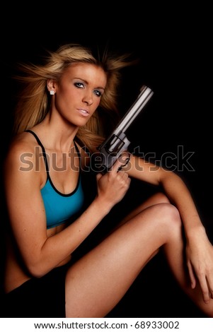 A woman in a blue halter top is serious and holding a gun.