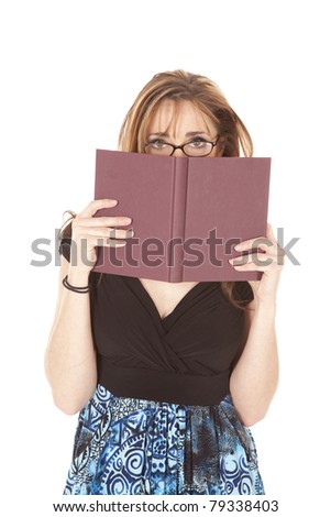 A woman peeking over the top of her book while she is wearing glasses.