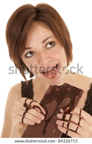 A woman licking her lips after taking a big bite of her chocolate covered chocolate candy bar.
