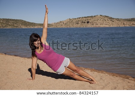A woman doing her yoga stretch on the beach with a smile on her face.