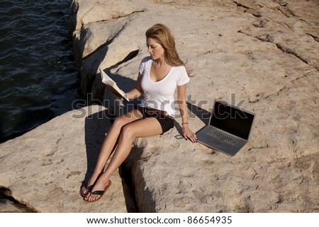 A woman in the outdoors trying to relax and read a book, but she is still locked to her computer.