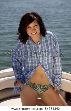 A woman kneeling on the back of the boat in her bikini wearing a plaid shirt.
