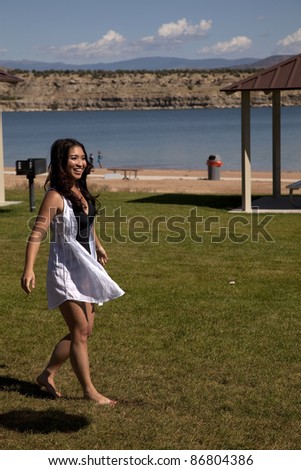 A woman walking around in the grass by the lake with  a smile on her face.