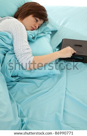 A woman wanting to sleep longer by pushing her snooze button on the alarm clock.