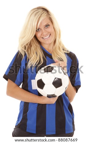 A woman with  a smile on her face holding on to a soccer ball in her soccer uniform.