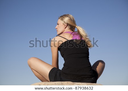 A woman stretching with her back to the camera in the outdoors.
