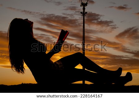 a silhouette of a woman leaning back holding on to a book.