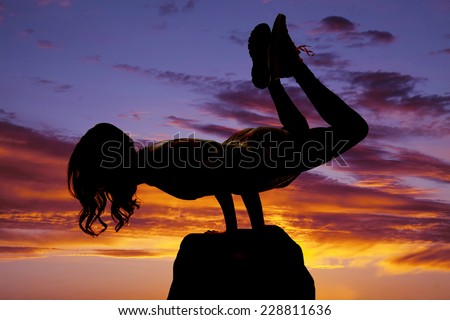 A silhouette of  woman doing a yoga strength pose on a rock.