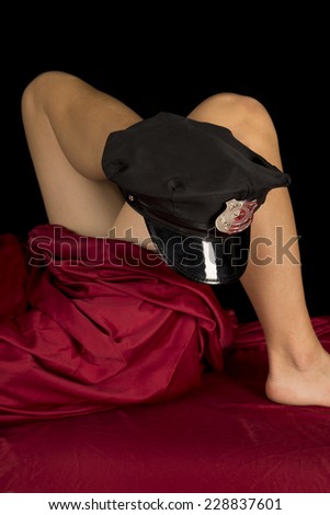 A woman laying under her sheet with a police hat on her foot.