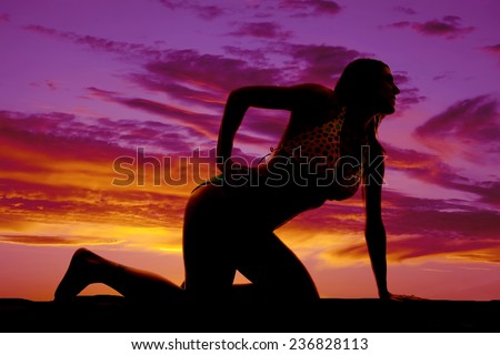 A silhouette of a woman kneeling on the beach.