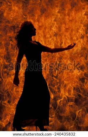 A silhouette of a woman in her fitted dress reaching out, with fire behind her.