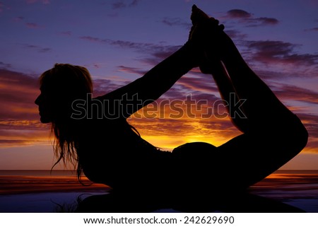 A silhouette of a woman reaching back to grab her legs in a yoga pose.