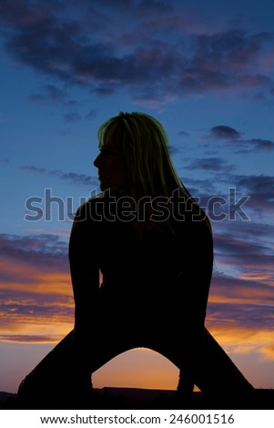 A silhouette of a woman on her knees stretching her legs looking to the side.