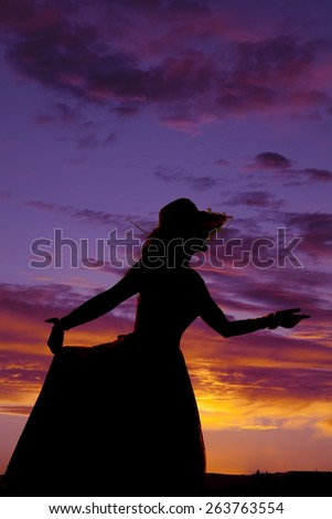 A silhouette of a woman reaching out in her formal dress with a hat.