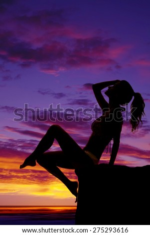 A silhouette of a woman sitting on a ledge in her bikini.