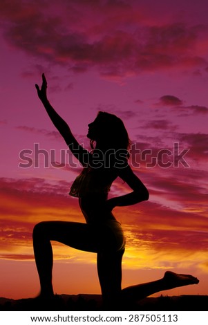 A silhouette of a woman kneeling in her bikini in the outdoors.
