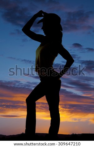 a silhouette of a woman in her western hat, touching the hat.