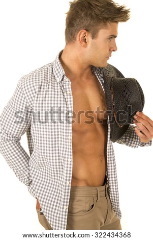 A cowboy with his shirt undone showing off his fit chest holding on to his western hat.