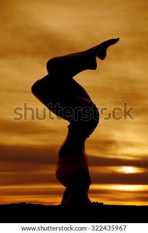 A silhouette of a woman doing a head stand in the outdoors.