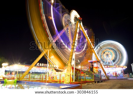 Colorful carnival Ferris wheel and gondola spinning in motion blurred at night in an amusement park