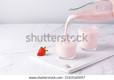 Pouring homemade fruit kefir, buttermilk or yogurt with probiotics. Yogurt flowing from glass bottle on light background. Probiotic cold fermented dairy drink. Trendy food and drink. Copy space Сток-фото © 