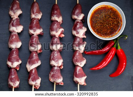 Ready to cook Duck Heart stringed on skewers BBQ with hot sauce and chili pepper. background.