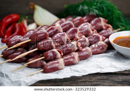 Ready to cook Duck Heart stringed on skewers BBQ with hot sauce and chili pepper. decorated with greens and vegetables. background.