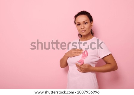Mixed race woman puts hands around pink ribbon on her pink T Shirt, for breast cancer campaign, supporting Breast Cancer Awareness. Concept of 1 st October Pink Month and women's health care