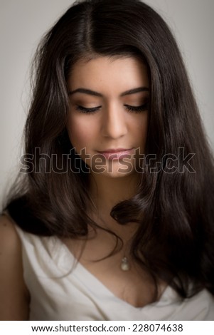Studio portrait of a beautiful young brunette woman with long curly hair looking down isolated against the background.