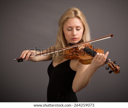 Studio portrait of a beautiful young blond female violin player playing a lovely tune isolated against a dark grey background.